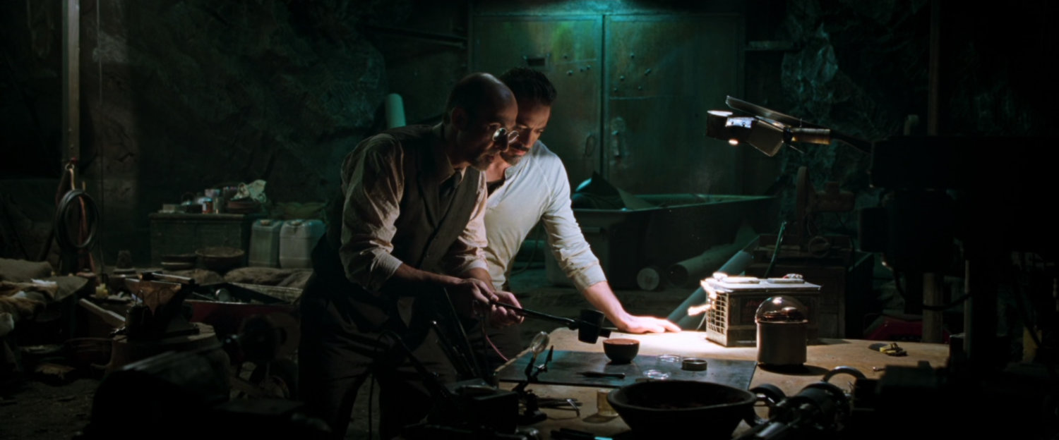 Tony Stark and Yinsen work in a dark cave.