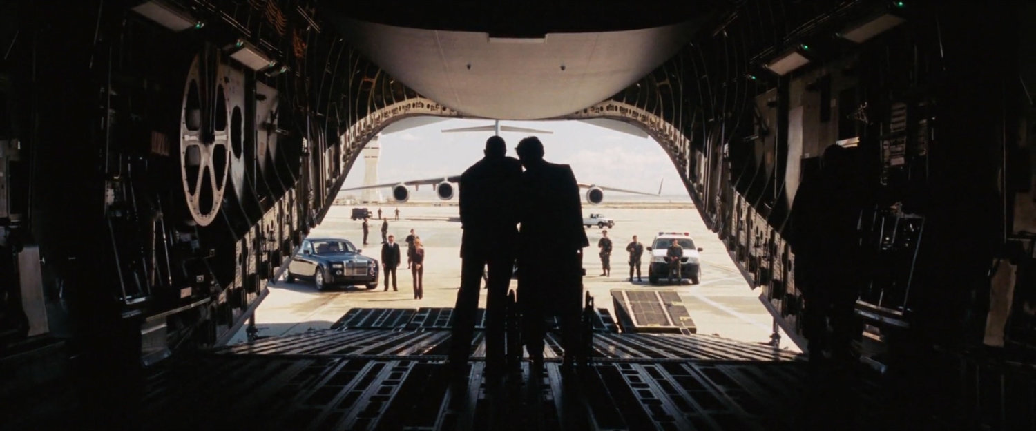 Silhouetted figures at the rear of a plane on an airfield.