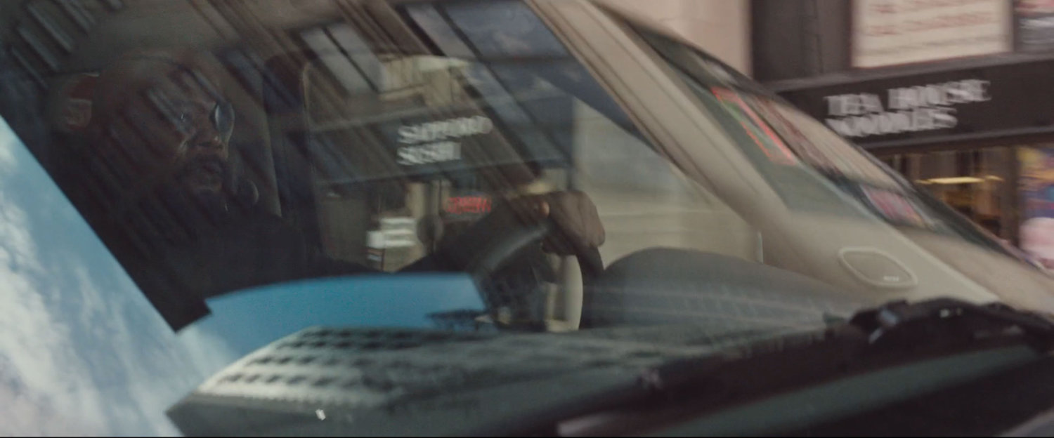 Nick Fury behind the wheel of SUV, driving on street.