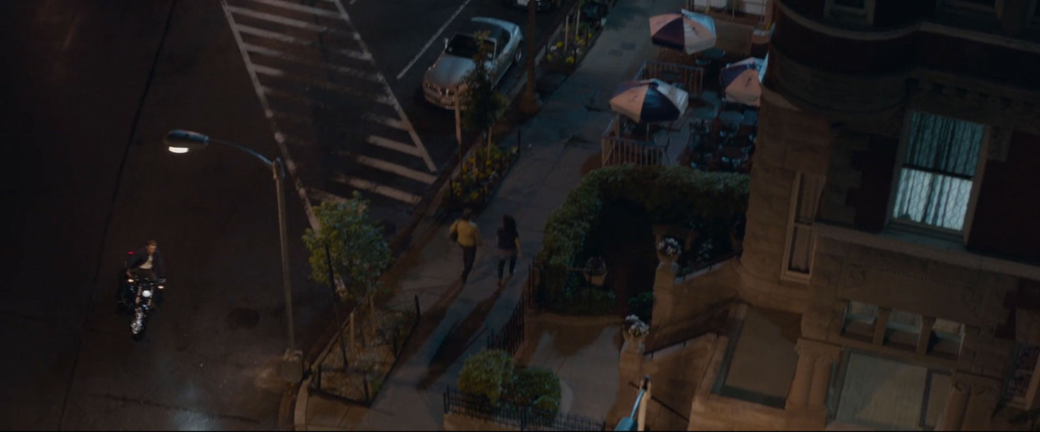 High angle of people walking on sidewalk and Steve Rogers pulling up on a motorcycle.