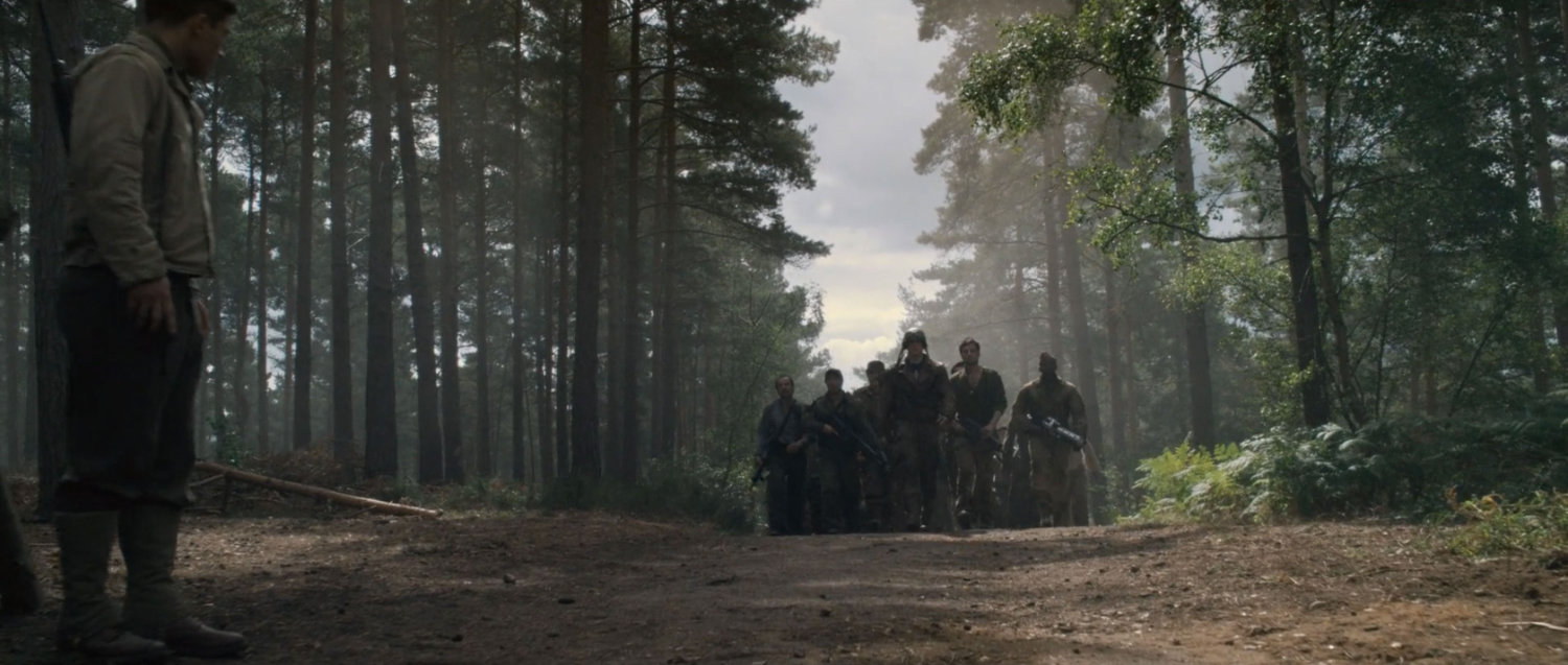 Steve Rogers leads a small group of men along a dirt road.