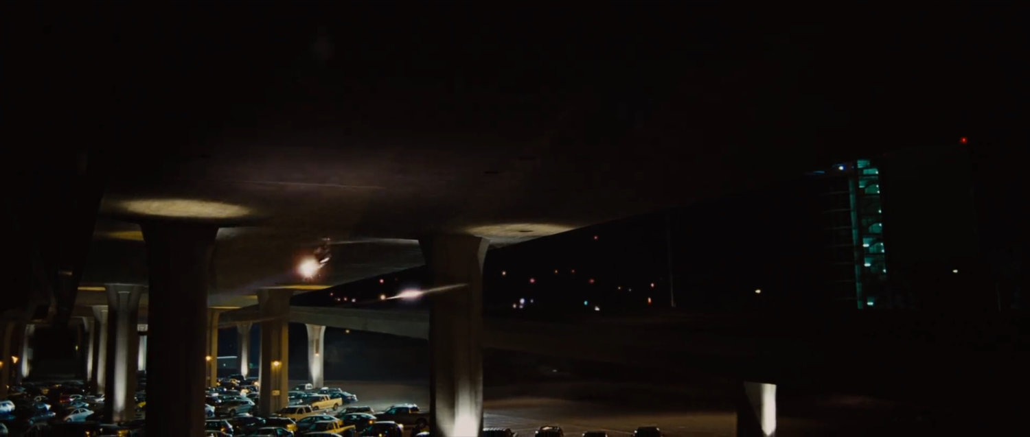 Nighttime under a freeway overpass with parked cars.
