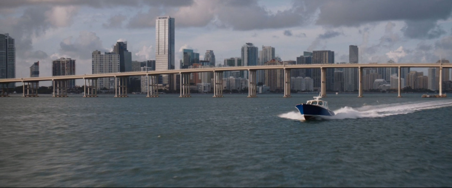 Speedboat crusing along water with bridge and Miami in background.