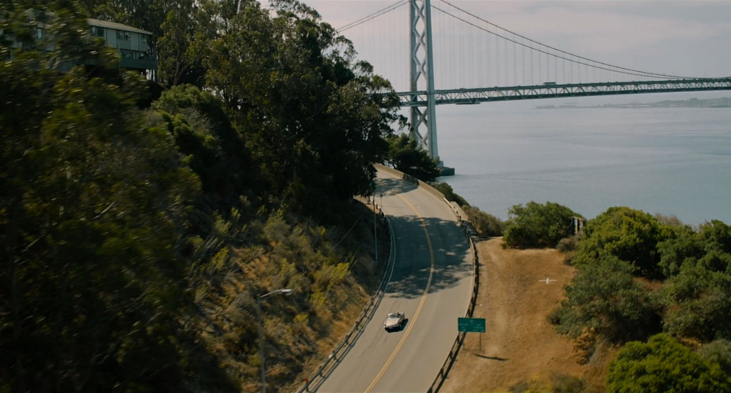 A car on winding road with Bay Bridge in background.