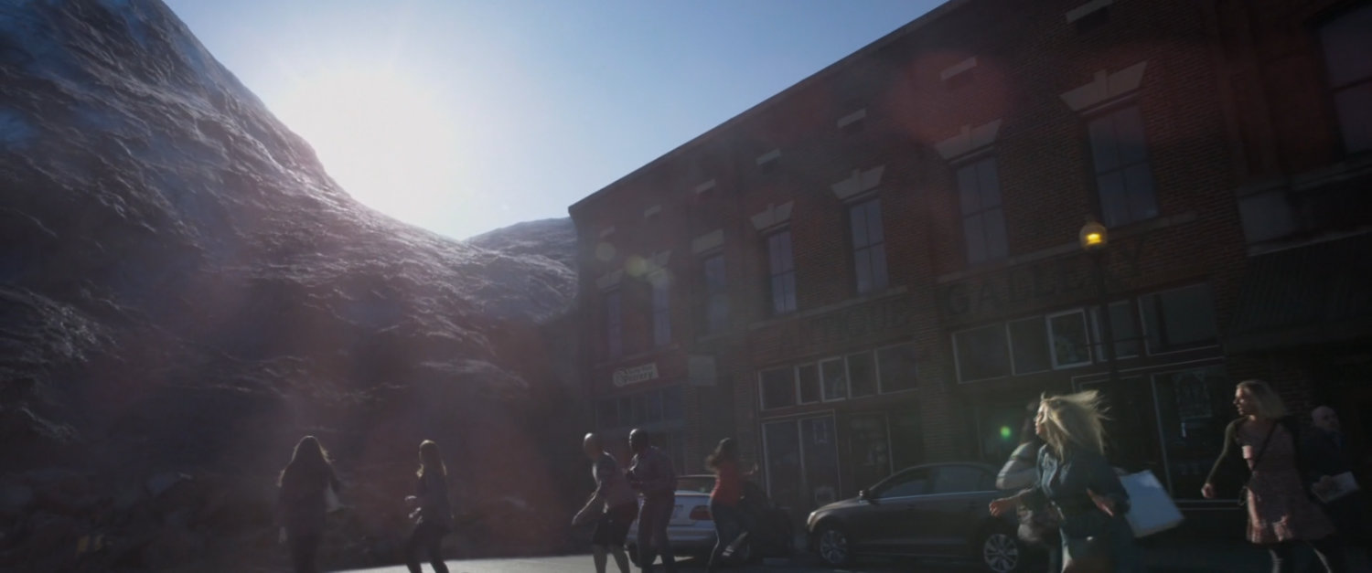 A giant alien spore towers over a crowd by a building.