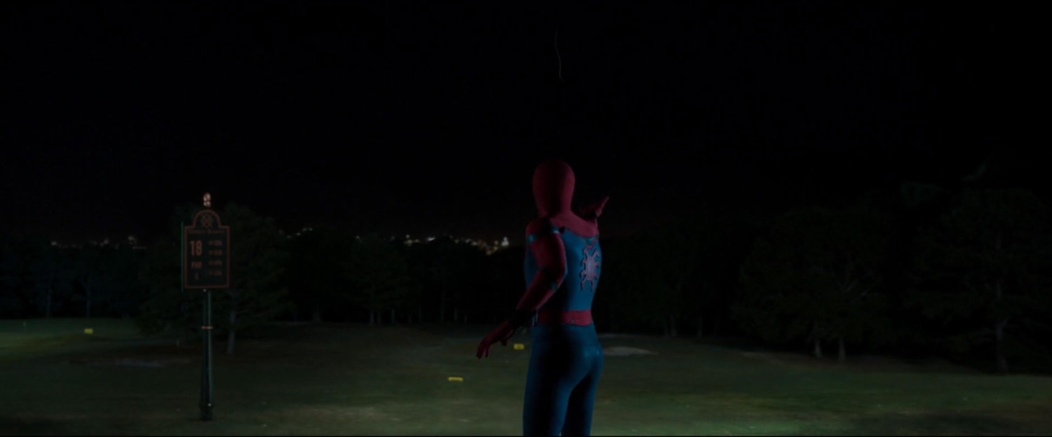 Spider-Man standing by the 18th hole of a golf course at night.