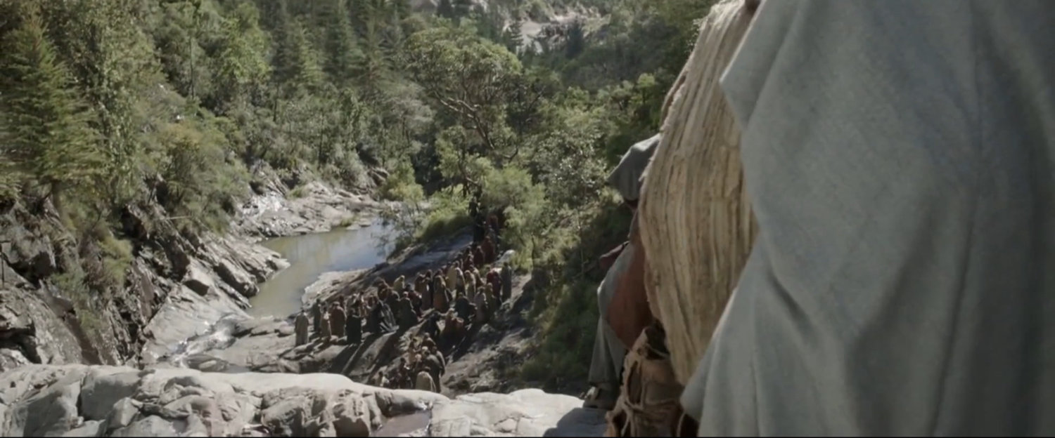 View of people on rocky path near waterfall.