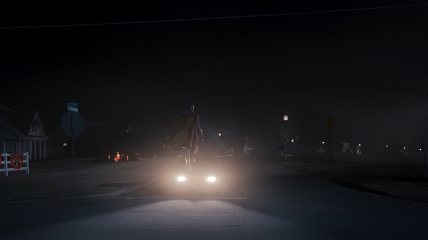 The Vision hovers in front of a car stopped at an intersection at night at the edge of Westview.