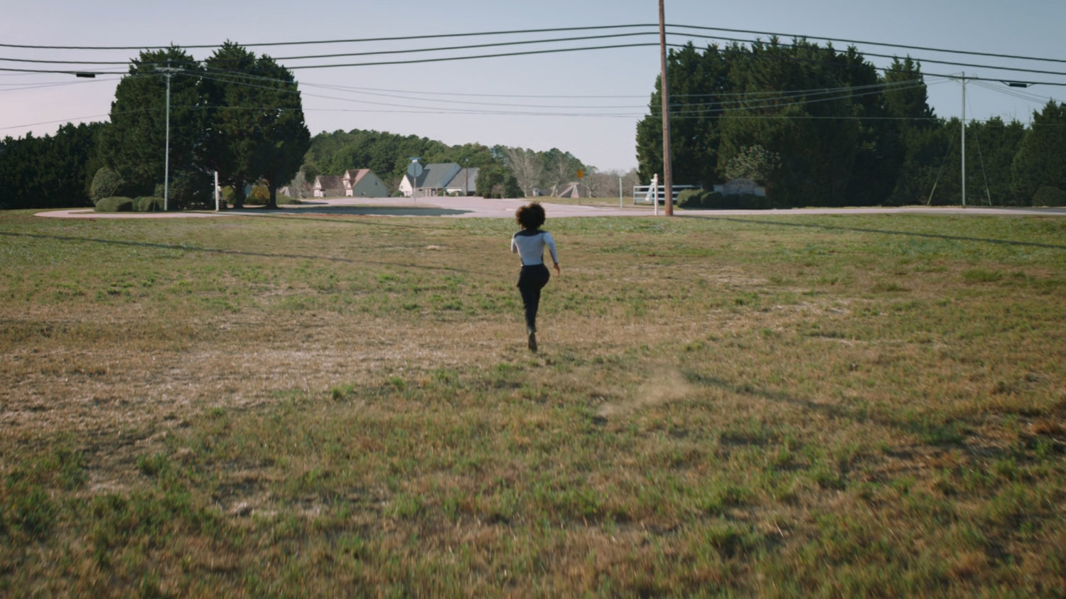 Monica runs across a field towards the edge of Westview.