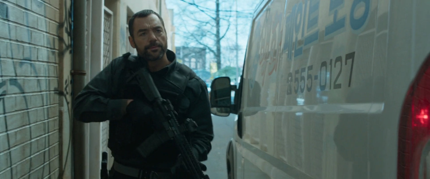 A man with gun walks past a white van.
