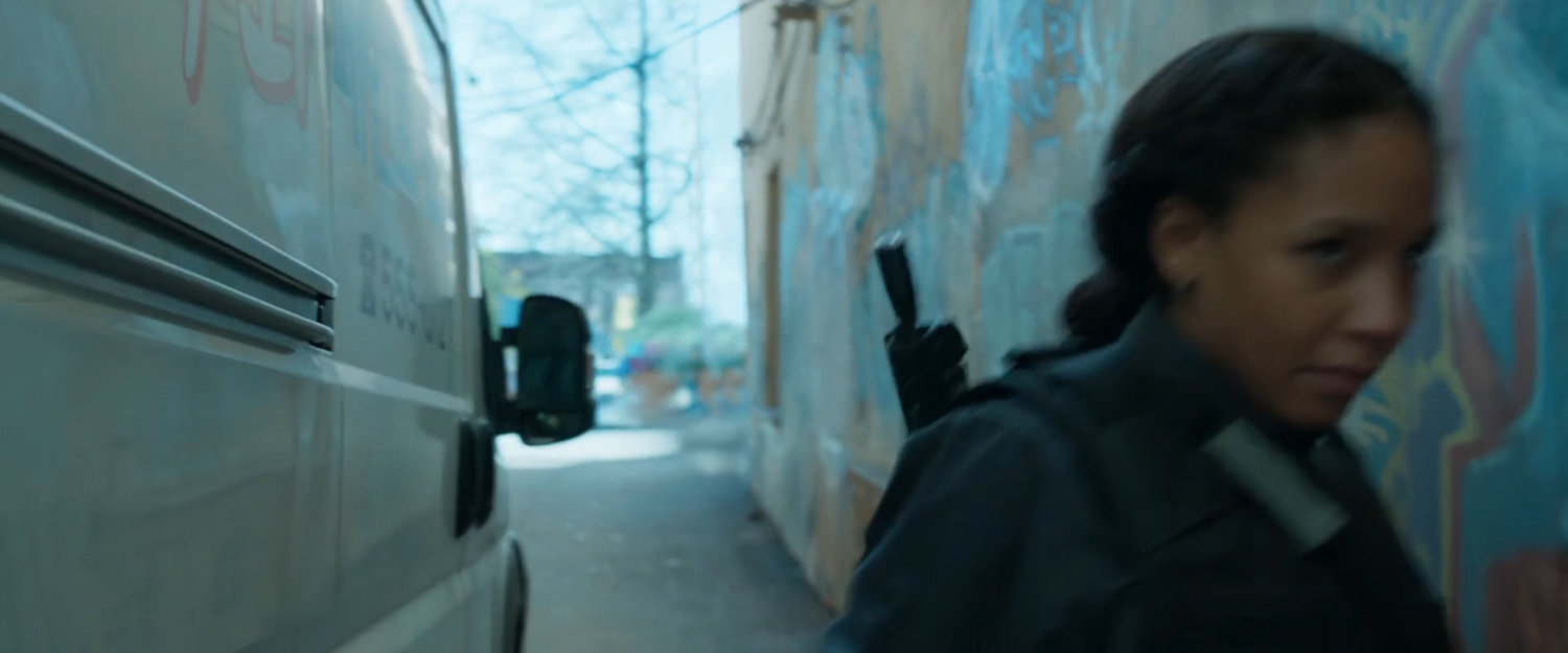 A woman with gun walks past a white van.