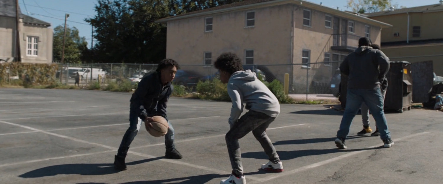 Two young boys playing basketball in a parking lot.