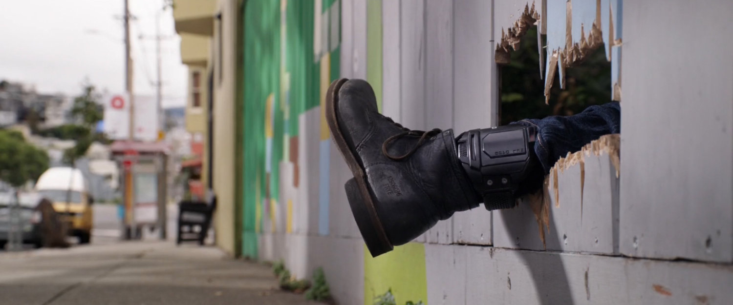 Foot with tracker sticking through wooden fence by sidewalk.