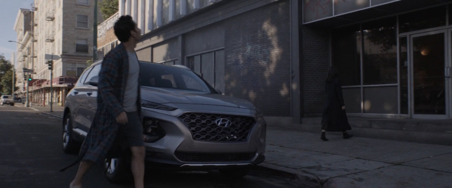 Scott Lang crossing in front of parked car towards building. 