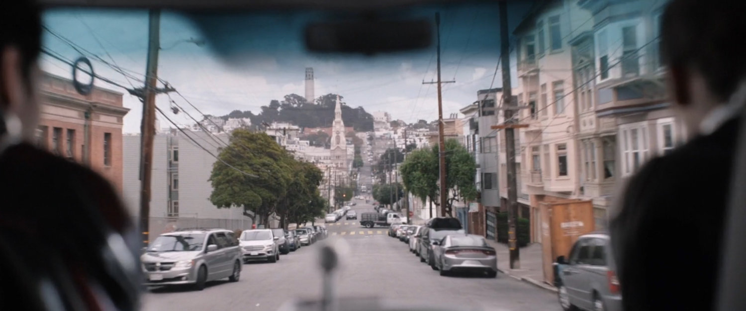 Cad driving on San Francisco street with Coit Tower in distance.