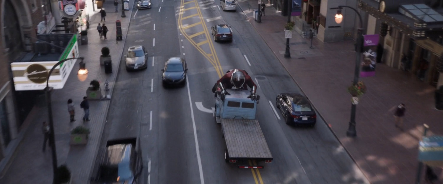Aerial view of Giant-Man pushing on front of flatbed truck to stop it.