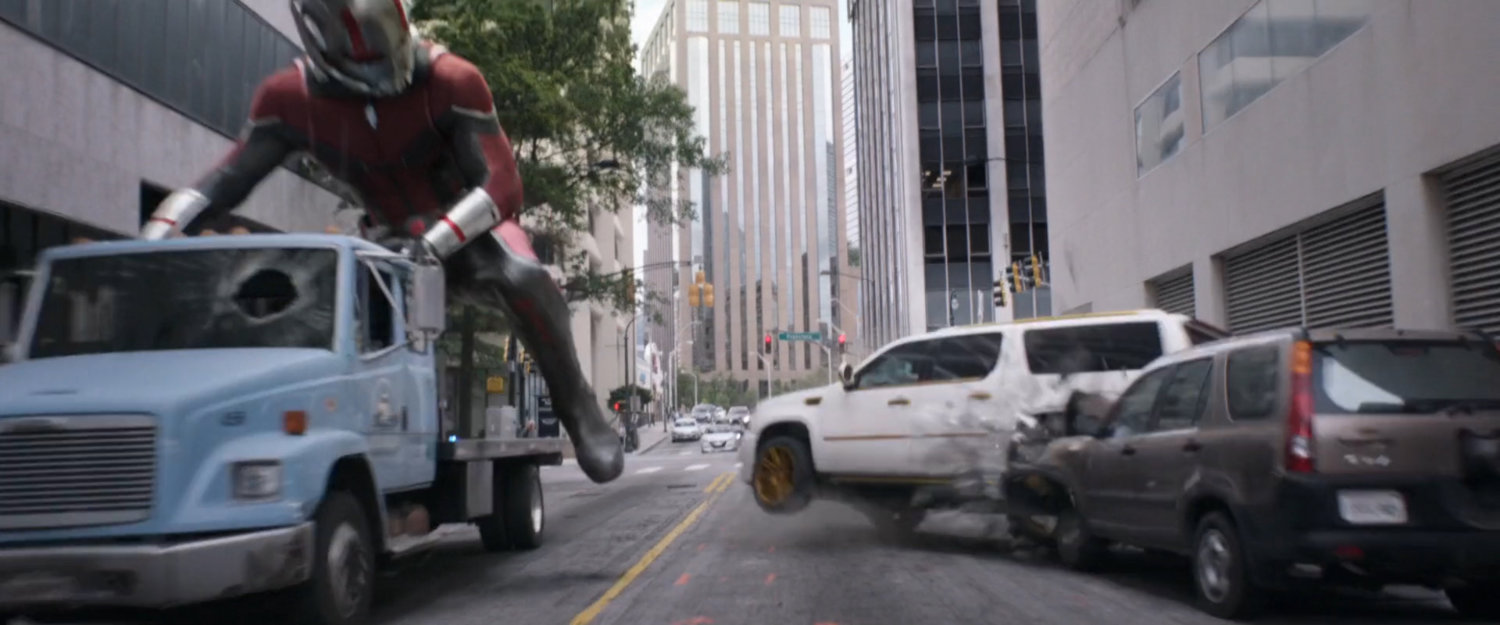 Giant-Man on flatbed truck kicks white SUV into parked cars.