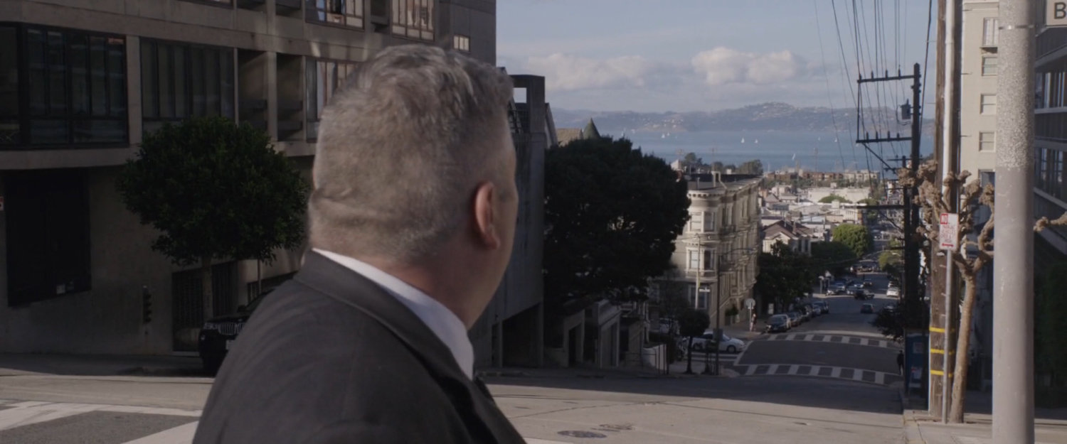 A man looks down a hilly street.