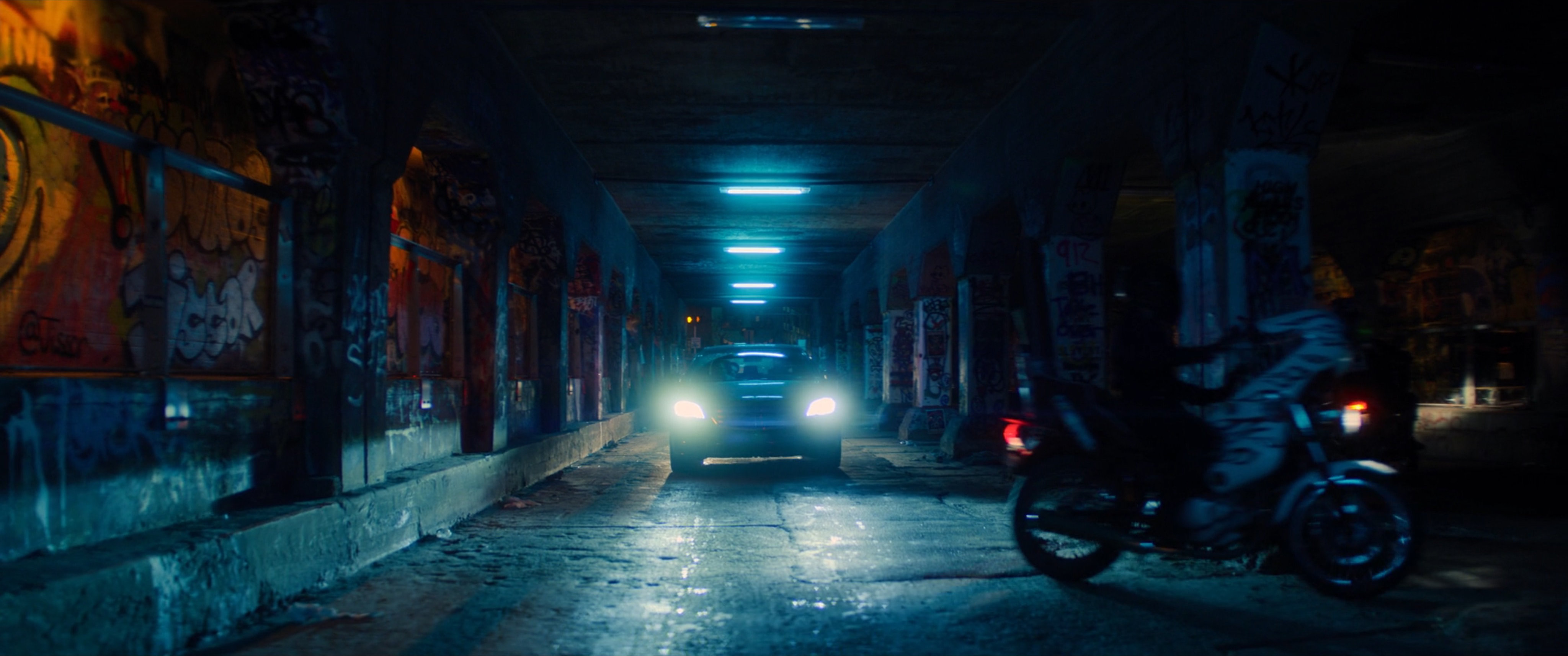 A sedan driving through a graffiti painted tunnel in Madripoor.