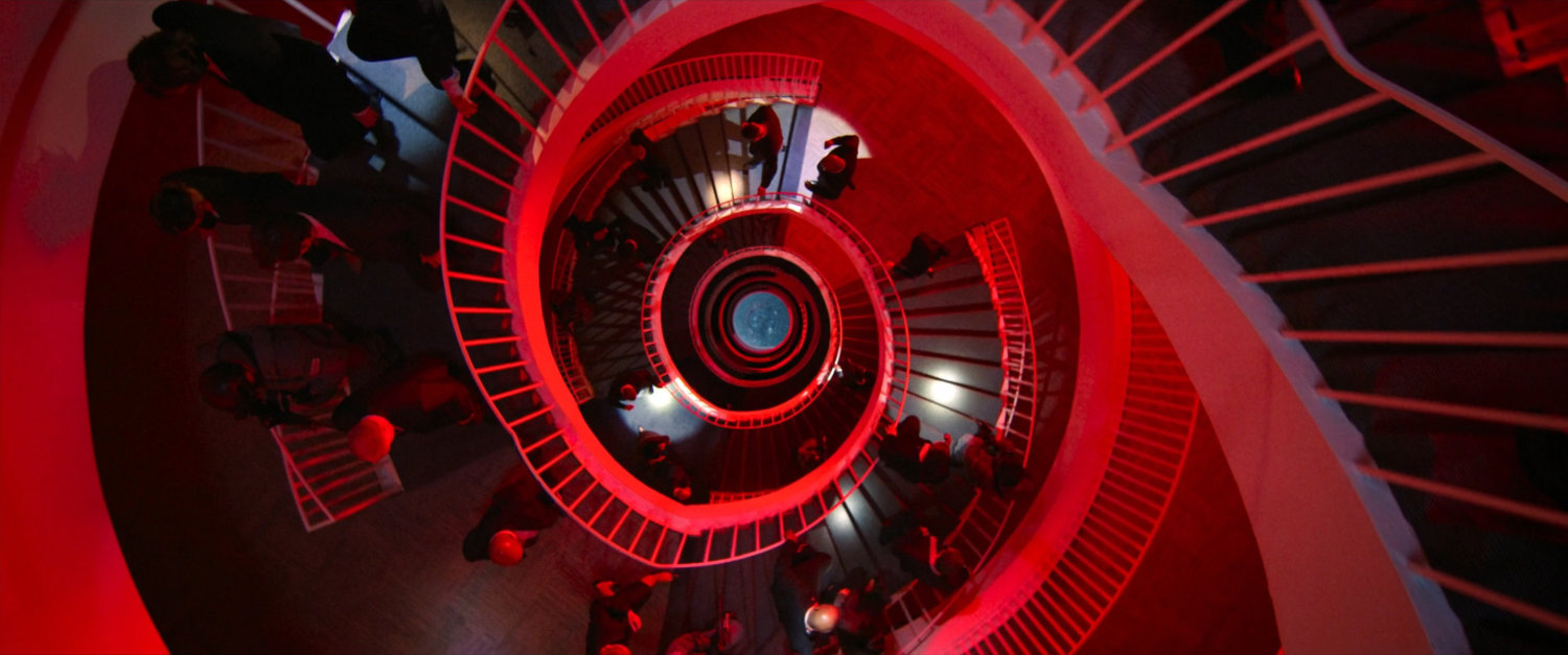 People descending circular stairs outside GRC Council Chamber bathed in red light.
