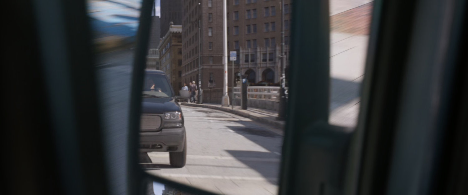SUV chasing van on San Francisco street, as seen in side mirror.