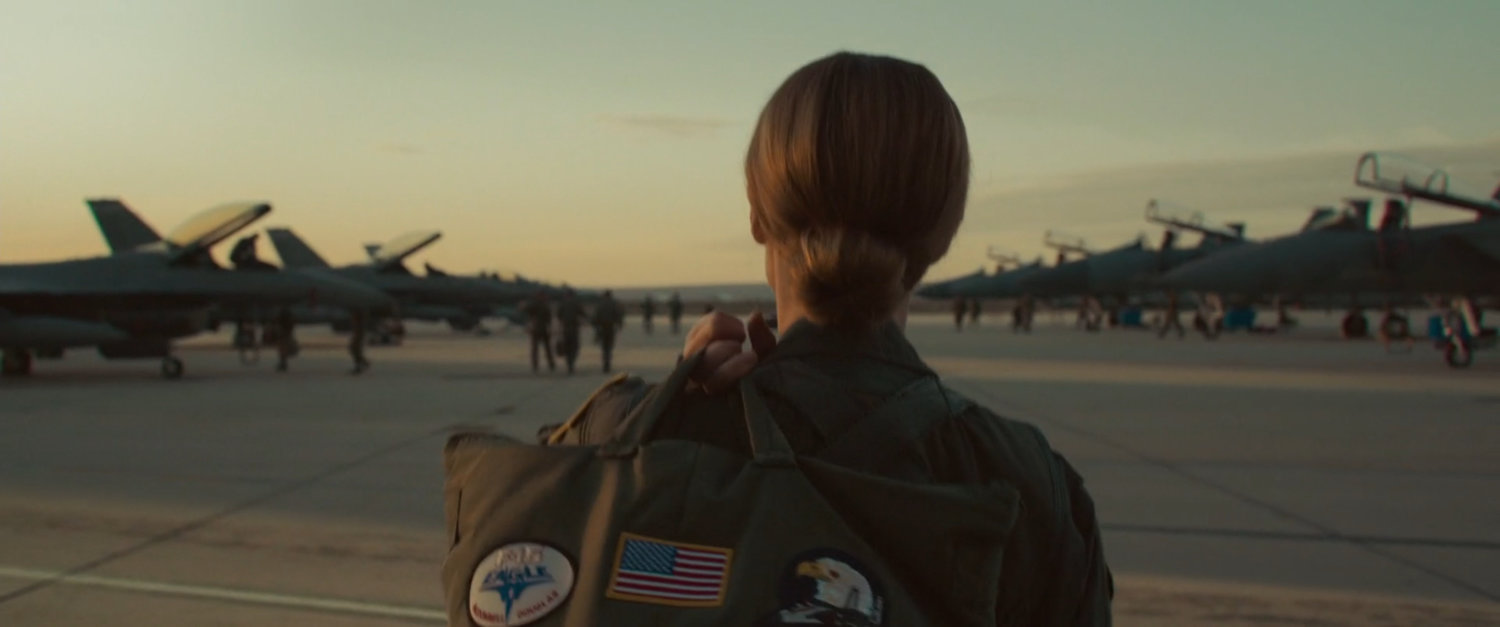 Carol Danvers walking toward rows of fighter planes at Edwards Air Force Base.