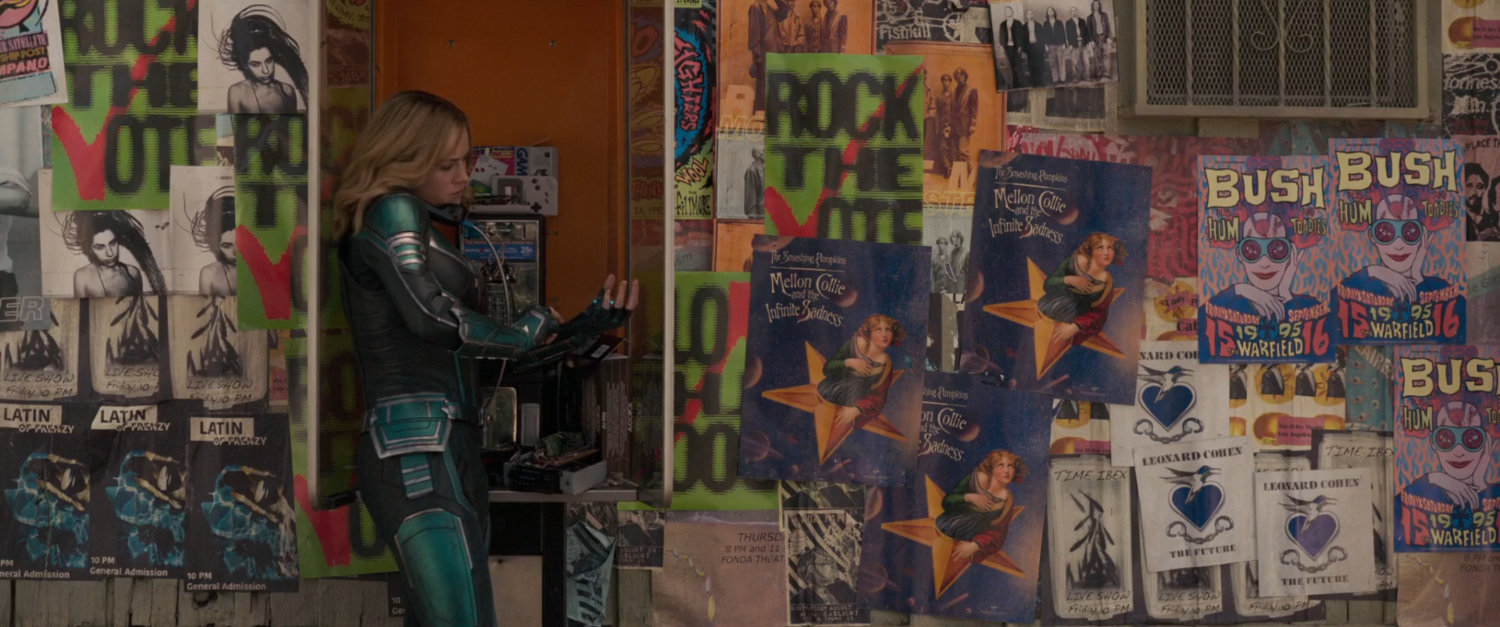 Vers on a pay phone surrounded by 90s-era advertisement posters.