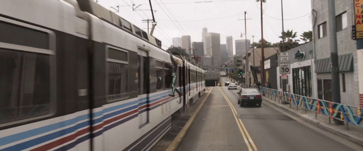 Vers hangs off side of Metro Train as it approaches tunnel with downtown Los Angeles in background.