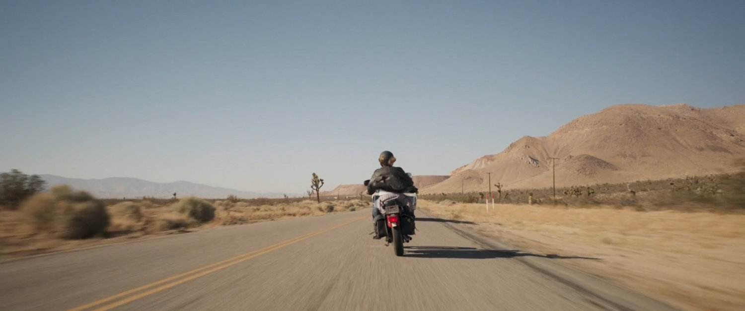 Vers riding motorcycle of desert highway.