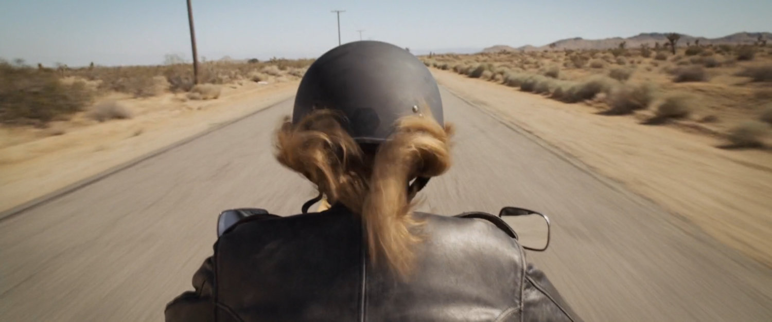Closeup of Vers riding motorcycle of desert highway.
