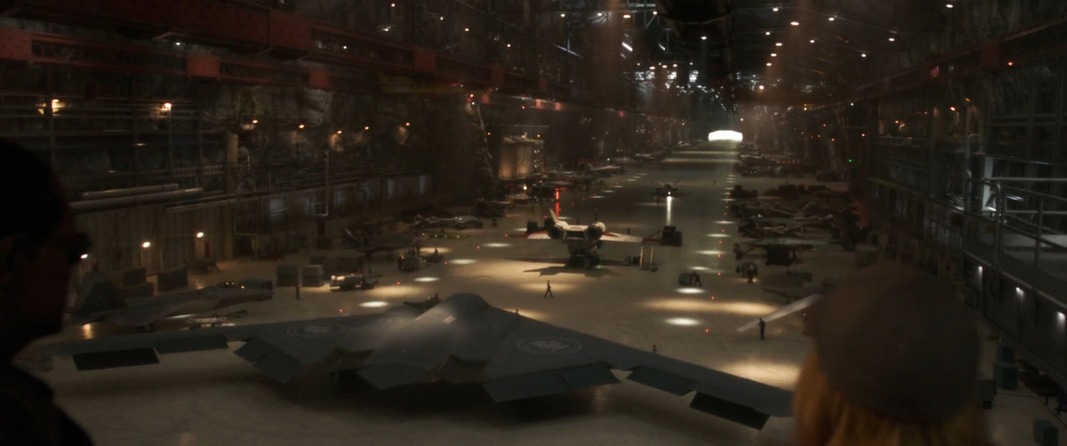 Nick Fury and Vers look out over vehicles in Project Pegasus hangar.