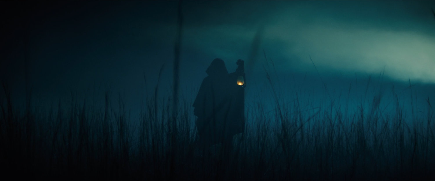 Silhouette with lantern in foggy Oklahoma field at night.