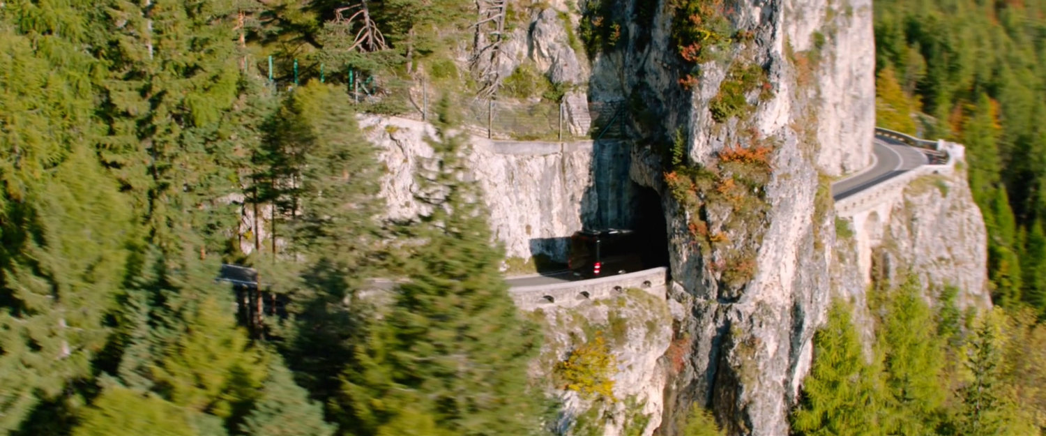 Aerial view of tour bus on winding mountain road entering small tunnel.