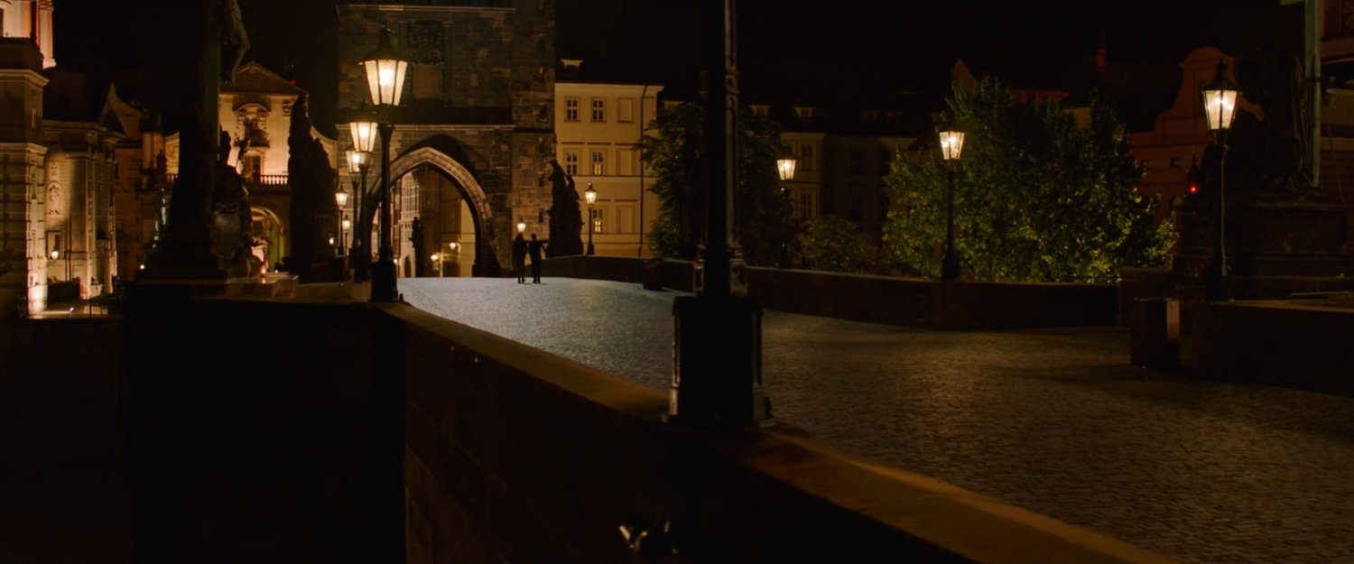 Two figures in the distance silhouetted on the Charles Bridge in Prague at night.