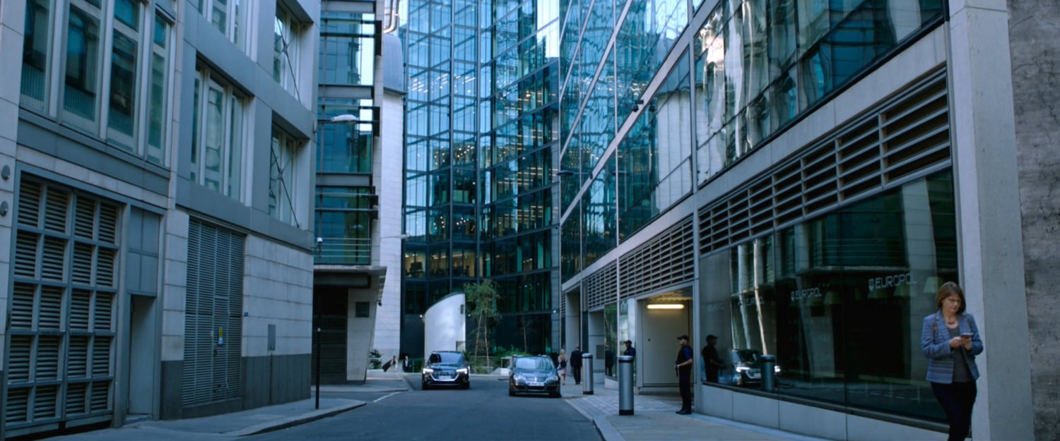 Cars on a street outside modern office buildings.
