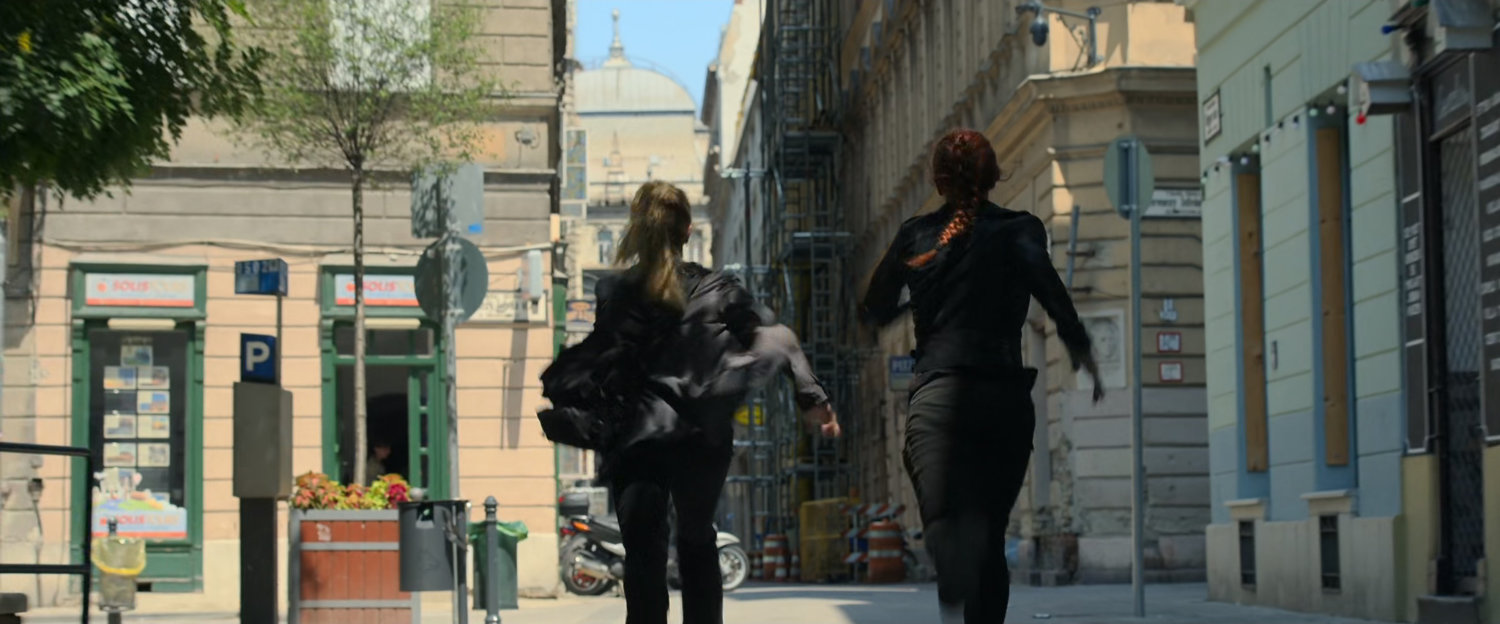 Yelena and Natasha run into an alley in Budapest.