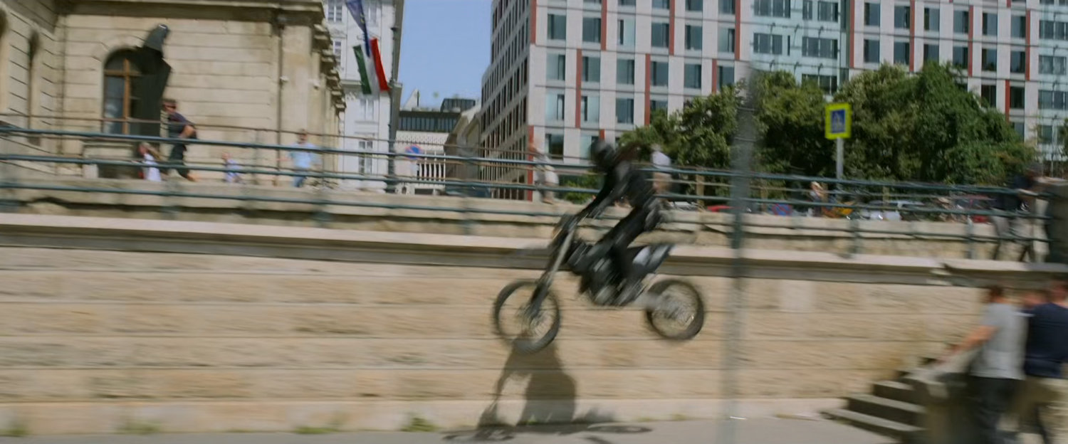 A motorcycle leaps off some stairs onto a lower roadway in Budapest.