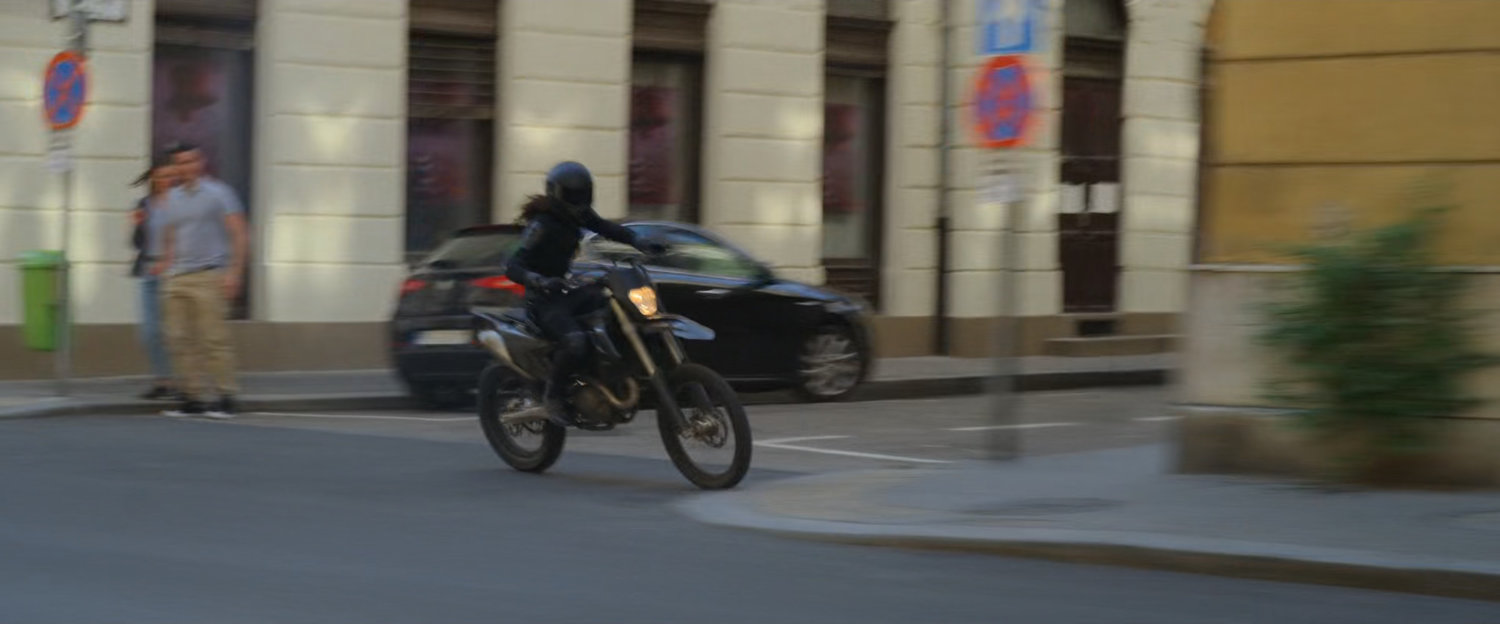 A motorcycle races down a Budapest street along a sidewalk.