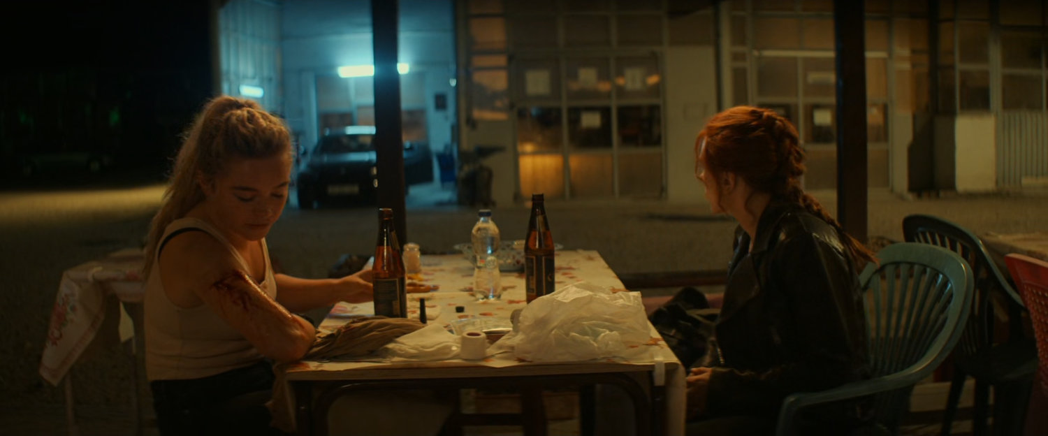 Natasha and Yelena eating at small table outside Varoil gas station.