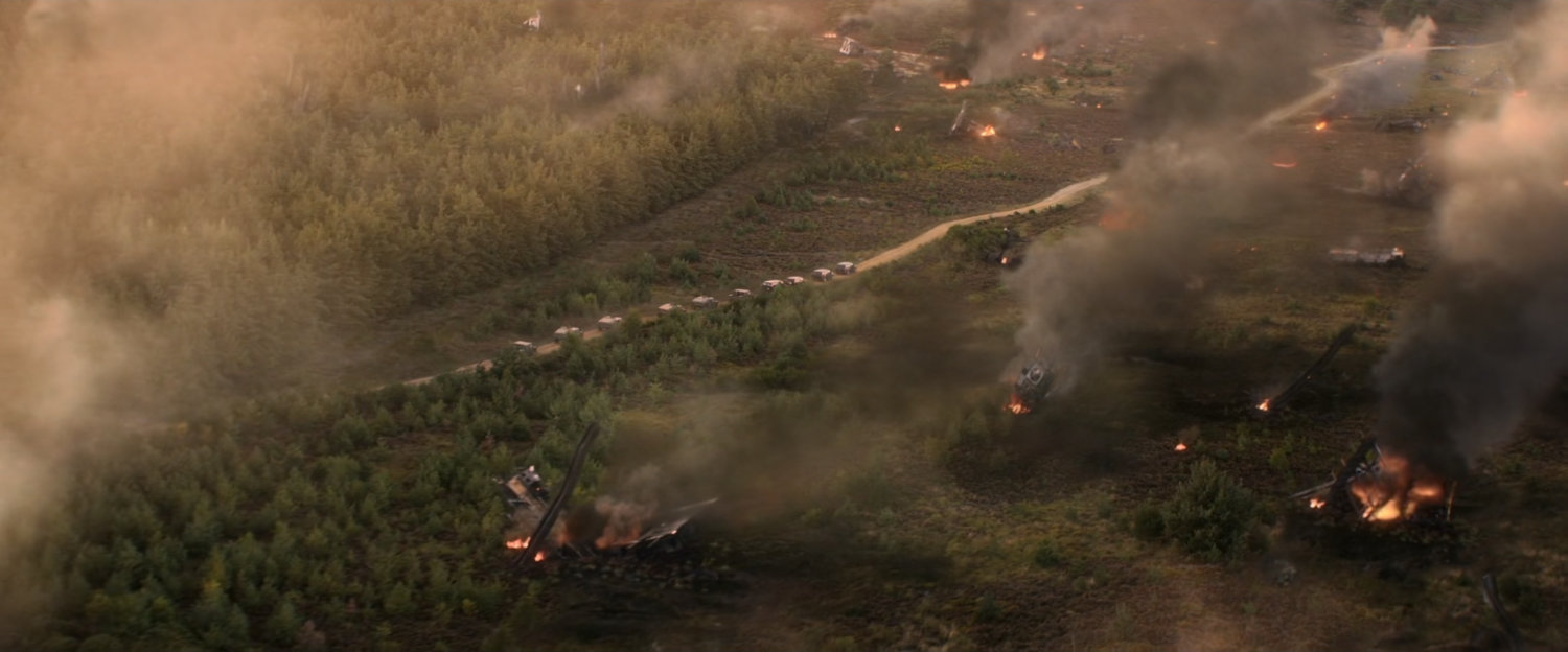 Aerial of field and road, lined with government cars, strewn with debris.