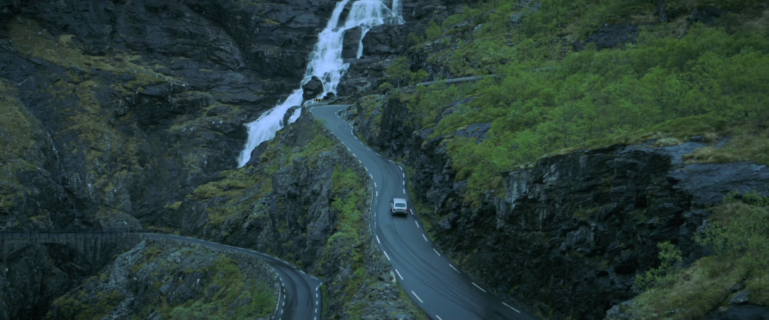A white car driving on a twisty Norwegian road.