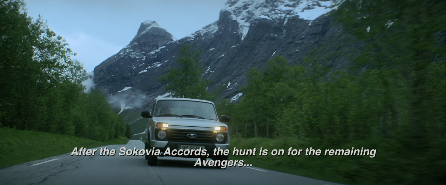 White car on a Norwegian roiad with snow capped mountains in background.