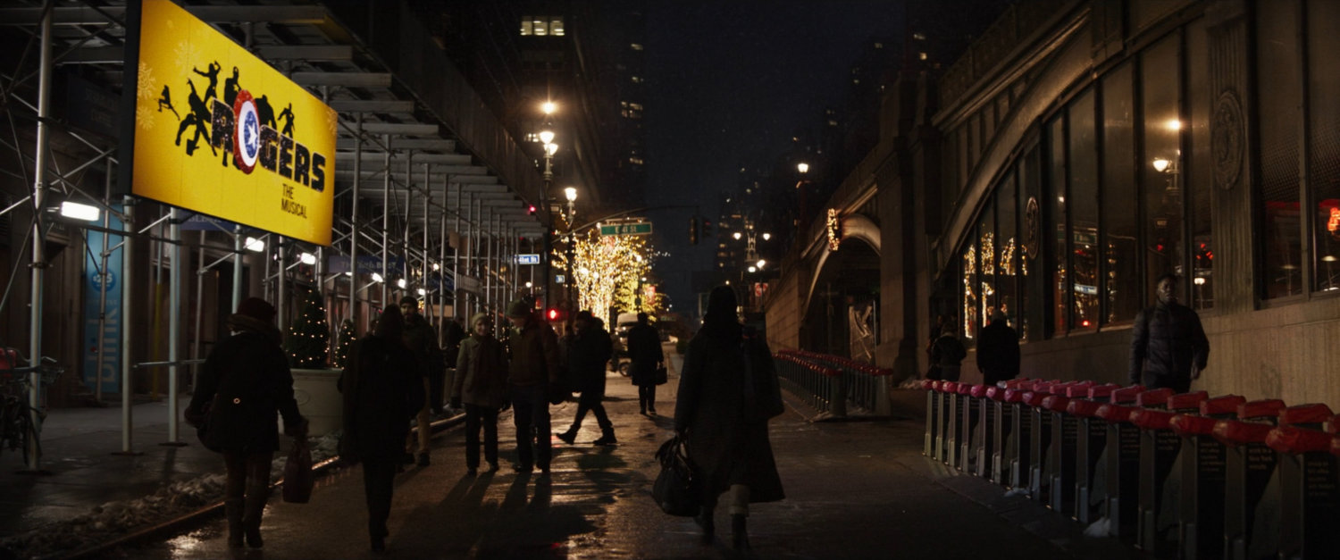 Kate walks through Pershing Square, where a Rogers the Musical sign hands on the wall.