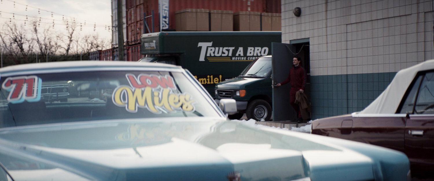 Kazi exits a building into the parking lot of Fat Man Used Cars.