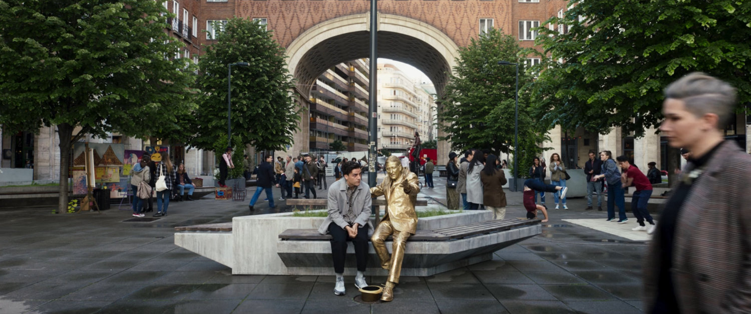 Steven sits on a bench next to the living statue in a London plaza.