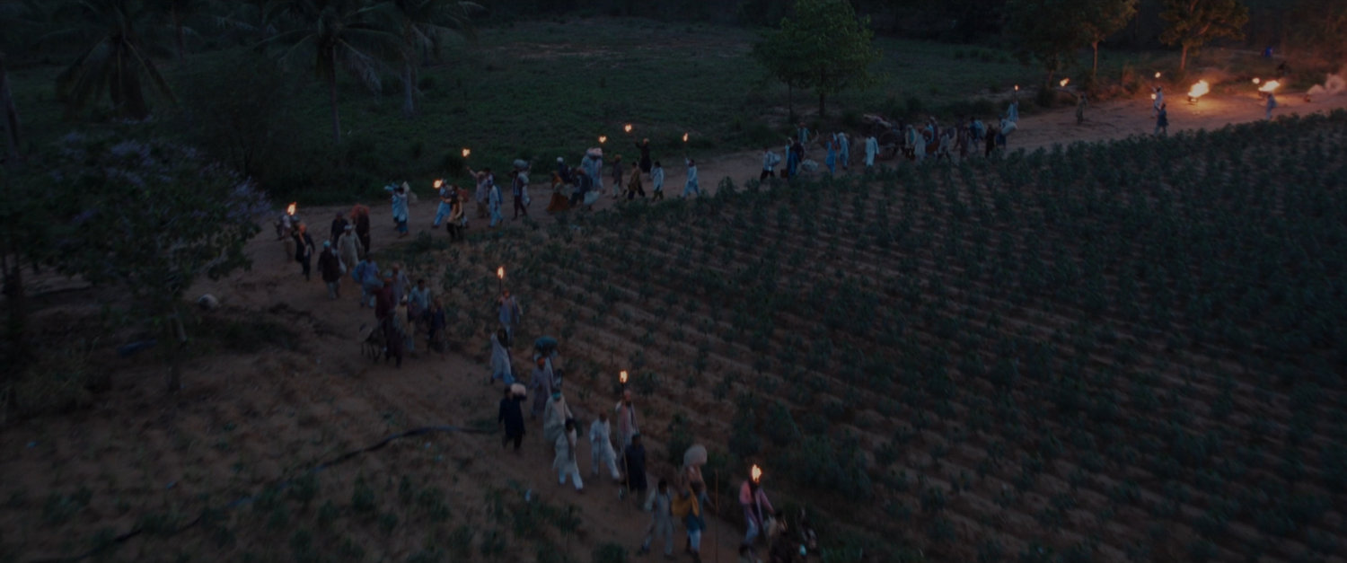 Villagers walking past crops in long procession.