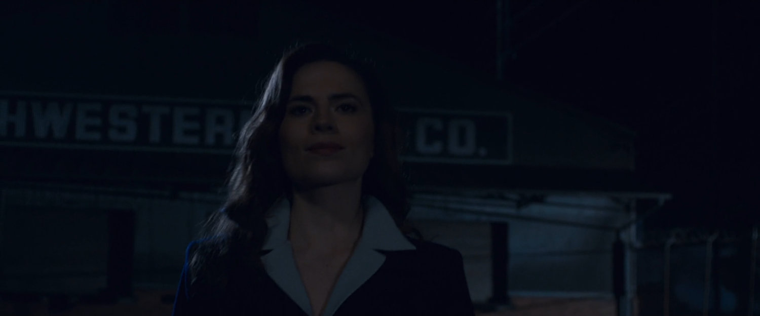 Nighttime shot of Peggy Carter walking towards warehouse.