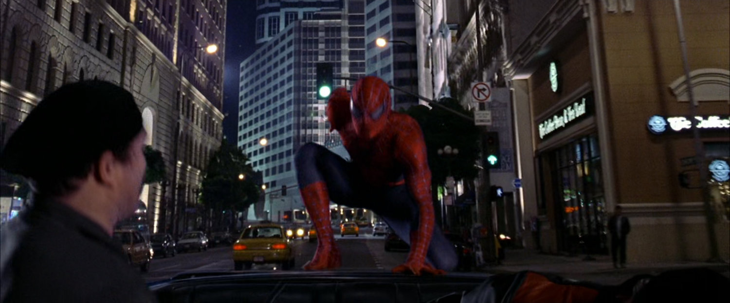 Spider-Man lands on robbers car at night.