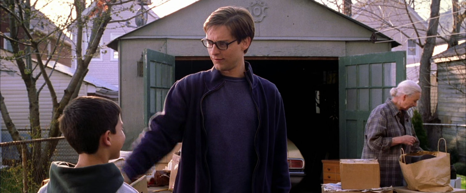 Peter Parker speaks with young boy in front of garage.