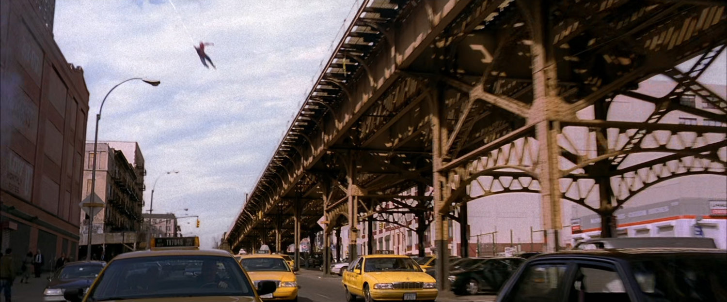 Spider-Man swings next to elevated train tracks.